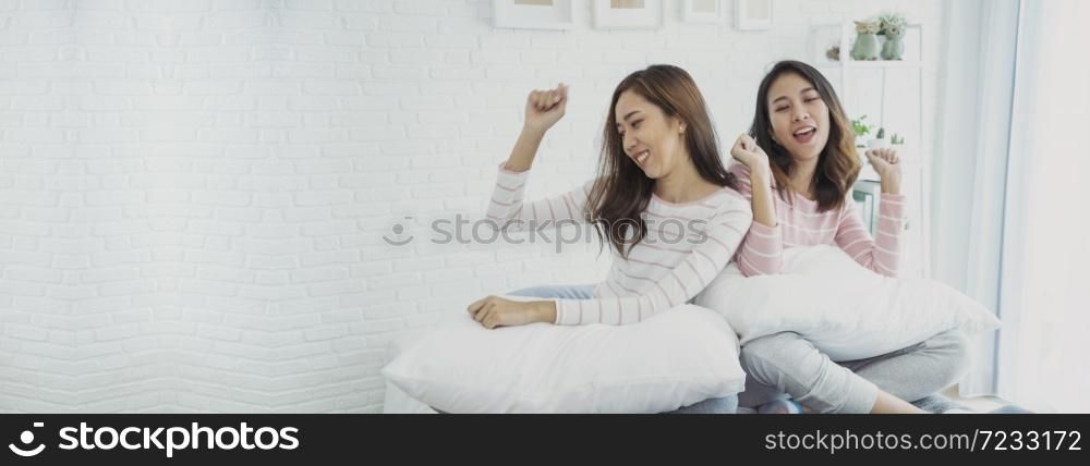 Two young women dance laughing together happy friendship smile with happiness in bedroom wear casual dress on bed. Happy girl friends dance to celebrate good news together at home. Woman joyful laugh