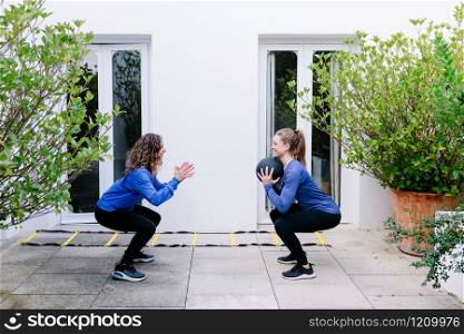 Two young women doing exercise together with medicine ball on a terrace