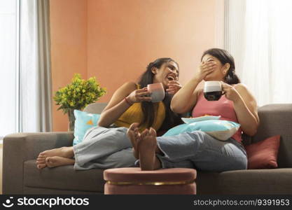 Two young women drinking coffee while relaxing on sofa in living room