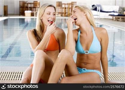 Two young women eating strawberries at the poolside