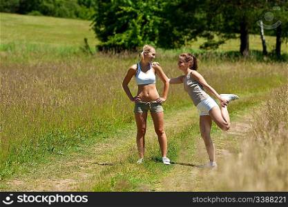 Two young women exercising in a meadow on sunny day
