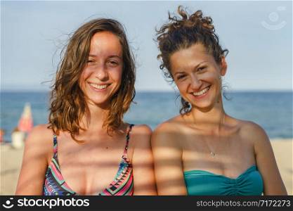 Two young women female girls friends in sunny summer or autumn day wearing bikini swim suit smiling with shadow on face happy on the vacation