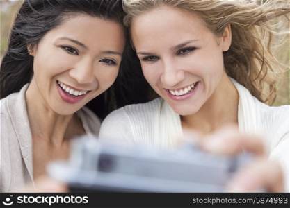 Two young women girls, one Asian Chinese, one blond, laughing taking selfie photograph with digital camera