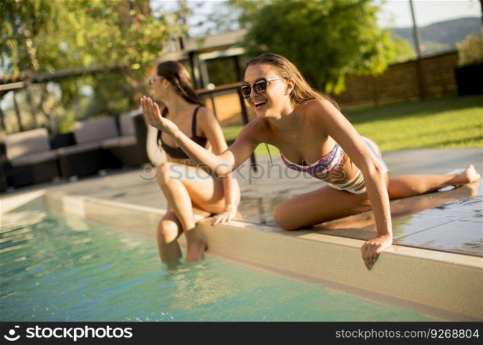 Two young women having fun by the swimming pool at hot summer day