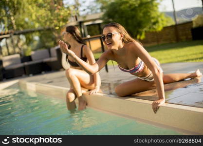 Two young women having fun by the swimming pool at hot summer day