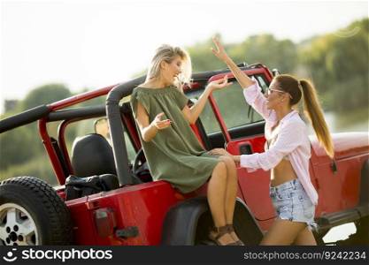 Two young women having fun on hood of a car by the lake at hot summer day