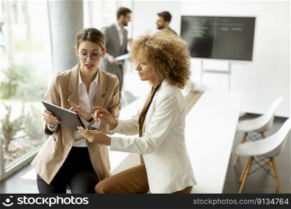 Two young women holding digital tablet and working in modern office