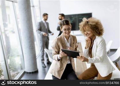 Two young women holding digital tablet and working in modern office