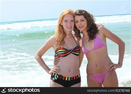 Two young women in bikinis posing in the surf