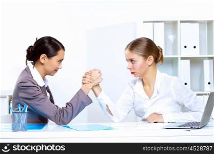 Two young women in business wear arm wrestling in office