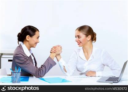 Two young women in business wear arm wrestling in office