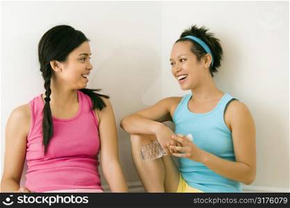 Two young women in fitness clothes sitting smiling and talking.