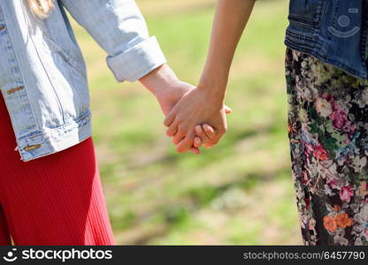 Two young women in walking holding her hands in urban park. Lifestyle concept. Front view.