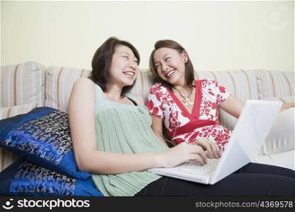 Two young women laughing and using a laptop