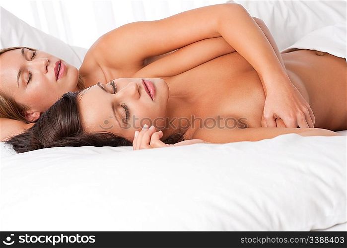 Two young women lying down in white bed and sleeping together naked