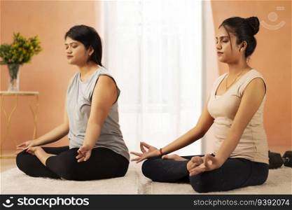 Two young women meditating in living room