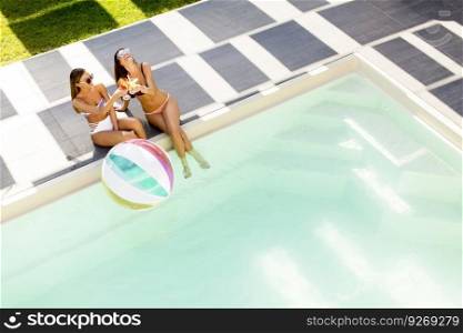Two young women relaxing by the swimming pool on a sunny day