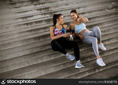 Two young women resting during training with bottle of water in urban environment