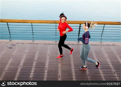 Two young women running on promenade by river in the morning