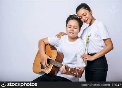 Two young women sat on a chair and played guitar.