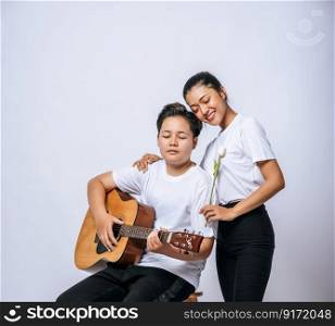 Two young women sat on a chair and played guitar.