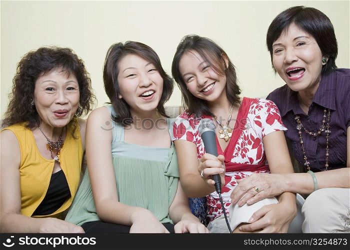 Two young women singing with their grandmothers into microphones