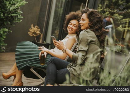 Two young women sit in the background watching at mobile phone and drinking cider