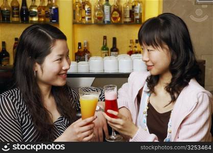 Two young women sitting at a bar counter raising a toast