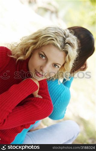 Two young women sitting back to back