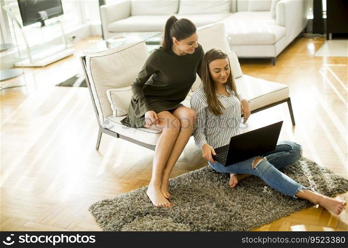 Two young women sitting in a room and using laptop