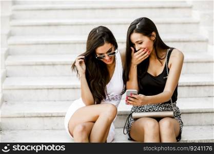 Two young women sitting on the stone steps outside and looking at the phone