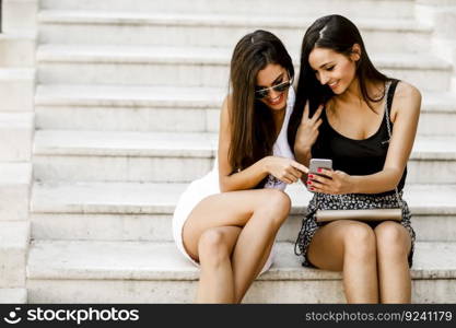 Two young women sitting on the stone steps outside and looking at the phone