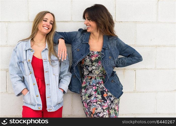 Two young women smiling in urban background. Happy girls on brick wall.