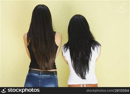Two young women standing against wall, backside view