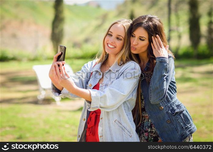 Two young women taking a selfie photograph in urban park. Lifestyle concept.