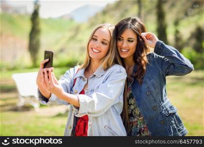 Two young women taking a selfie photograph in urban park. Lifestyle concept.