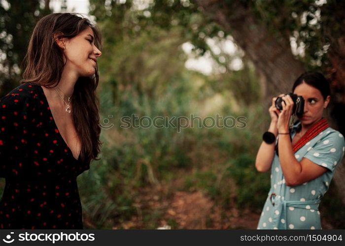 Two young women taking photos each other in the forest among trees wearing dresses and sneakers