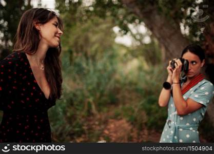Two young women taking photos each other in the forest among trees wearing dresses and sneakers