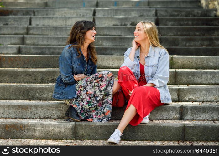 Two young women talking and laughing on urban steps. Two girls wearing casual clothes. Lifestyle concept.