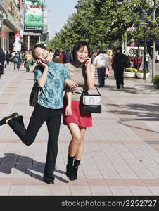 Two young women talking on mobile phones in a street