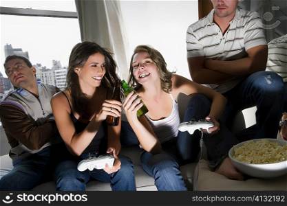 Two young women toasting with beer bottles and two young men sitting beside them