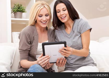 Two Young Women Using Tablet Computer At Home on Sofa