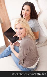 Two Young Women Using Tablet Computer At Home on Sofa