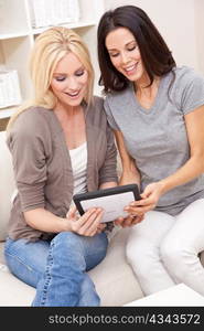 Two Young Women Using Tablet Computer At Home on Sofa