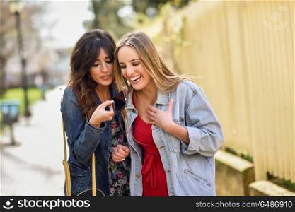 Two young women using the voice recognition of the phone outdoor. Two young women using the voice recognition of the phone. Girls sending a voice message with smart phone outdoors.