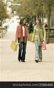 Two young women walking on footpath and carrying shopping bags