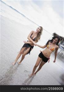 Two young women walking on the beach and smiling