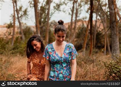 Two young women walking through the forest wearing dresses