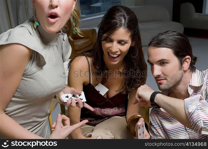Two young women with a young man playing cards