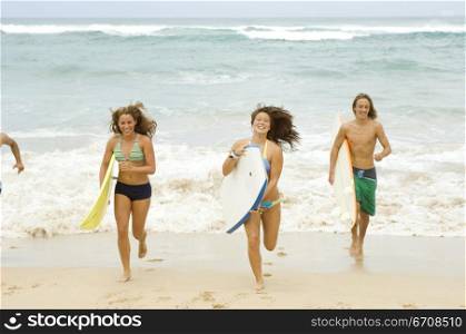 Two young women with a young man running on the beach